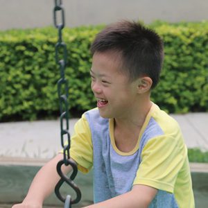 boy with down syndrome laughs while swinging