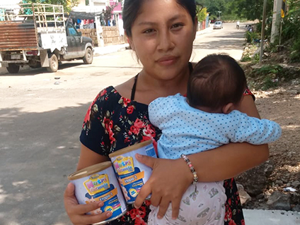 mama holding her infant and 2 cans of formula given out through 